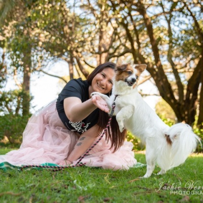 woman-wearing-pink-frilly-dress-playing-with-small-fluffy-dog-in-park