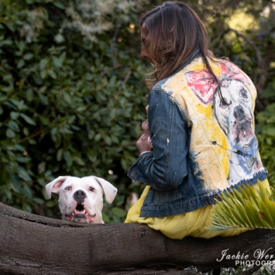 white-pitbull-blue-eye-peering-over-log-with-woman-sitting-nearby